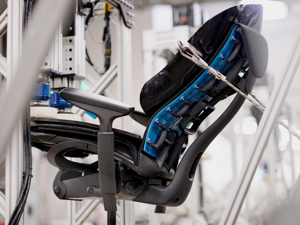 An Embody Gaming Chair, shown from the side, in a testing machine at the Herman Miller manufacturing site.